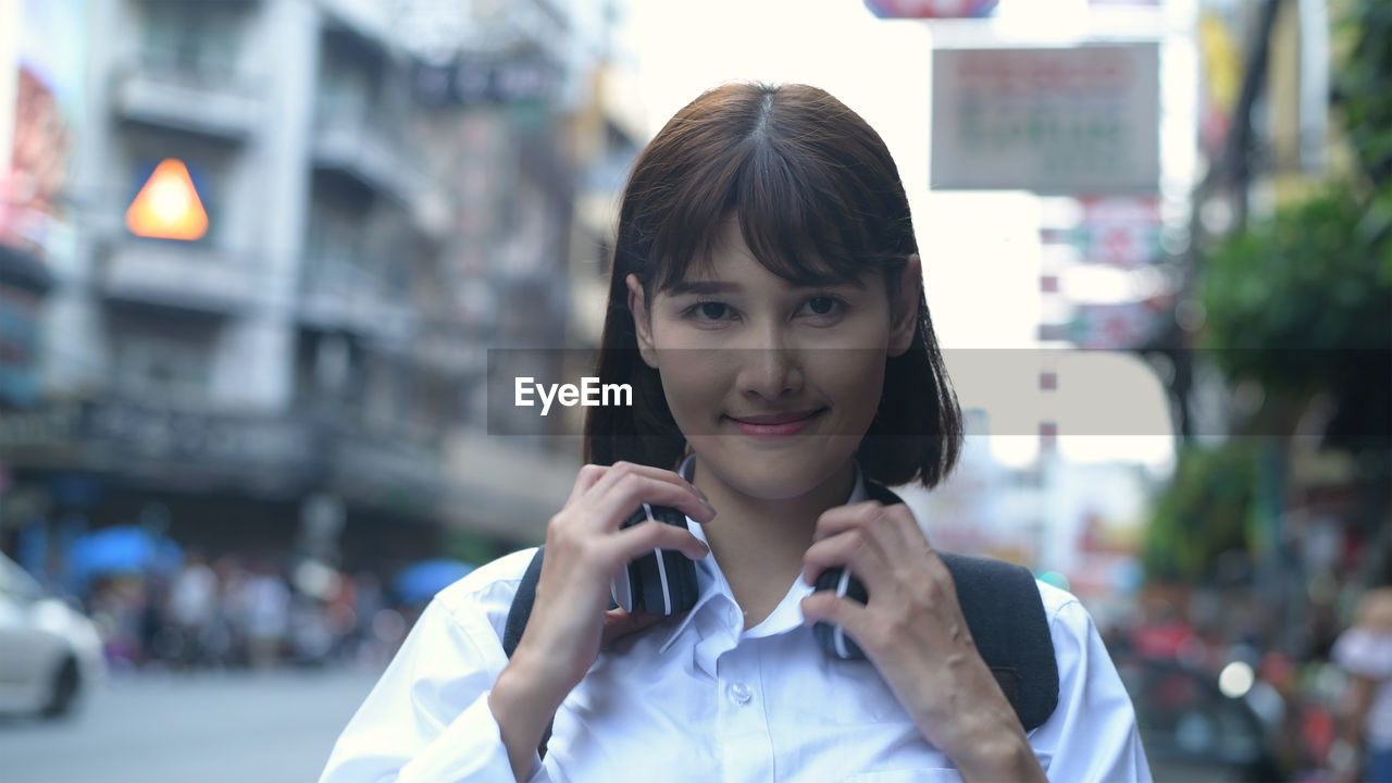 Portrait of smiling woman with headphones standing in city