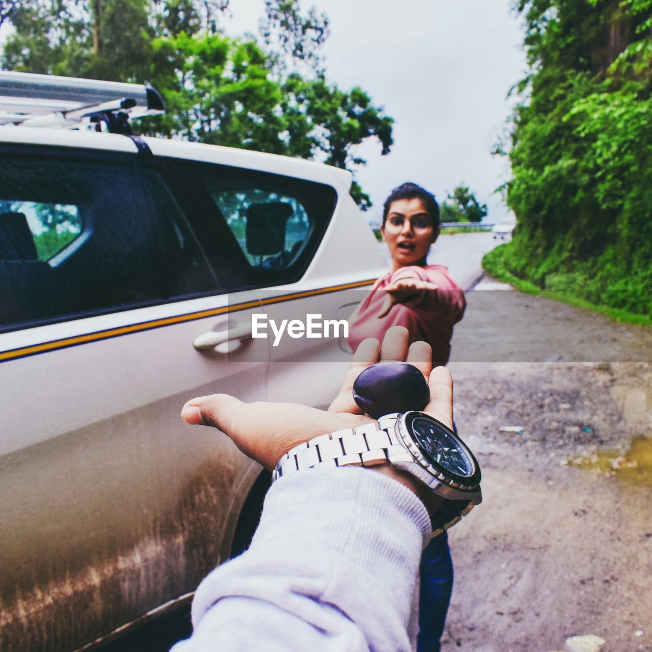 Cropped hand of man offering fruit to woman while standing by car on road