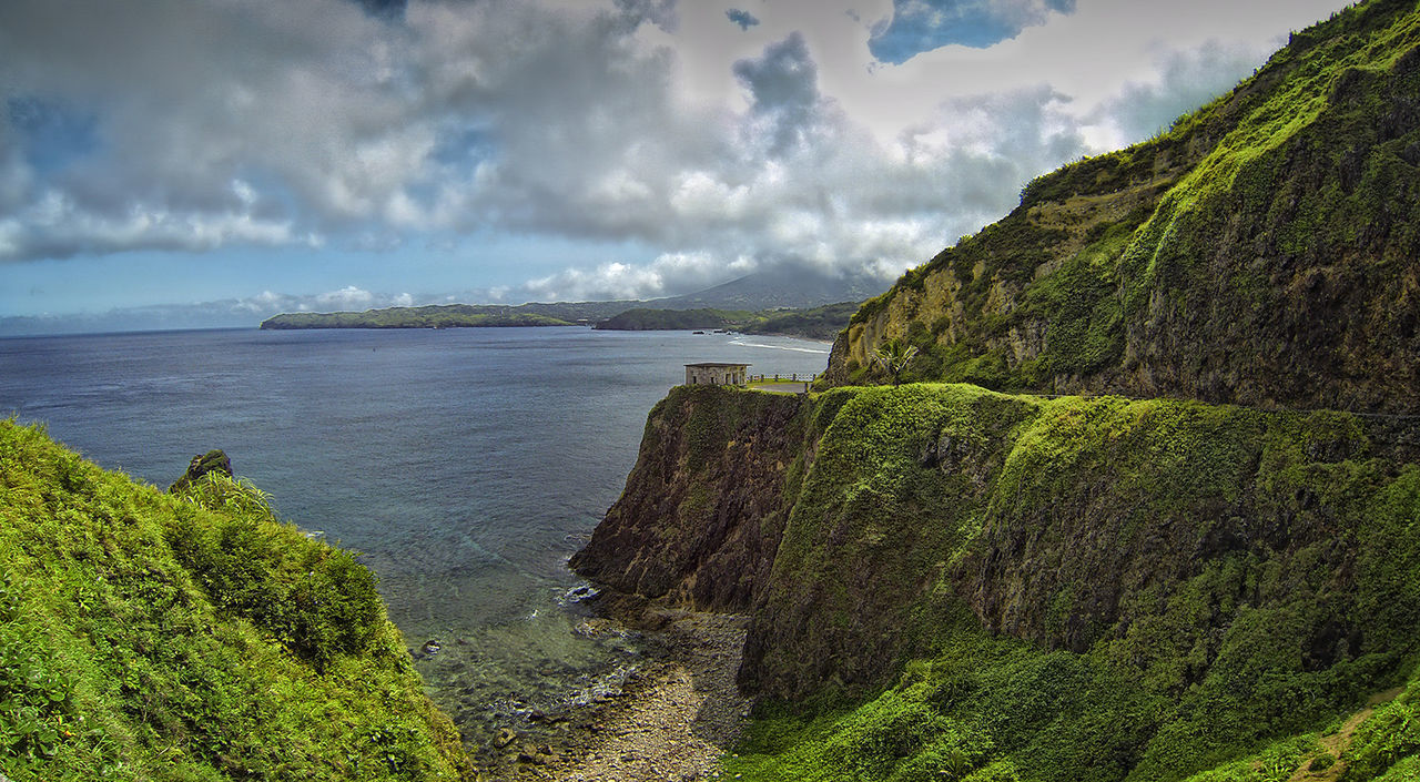 Scenic view of green mountains by sea against cloudy sky