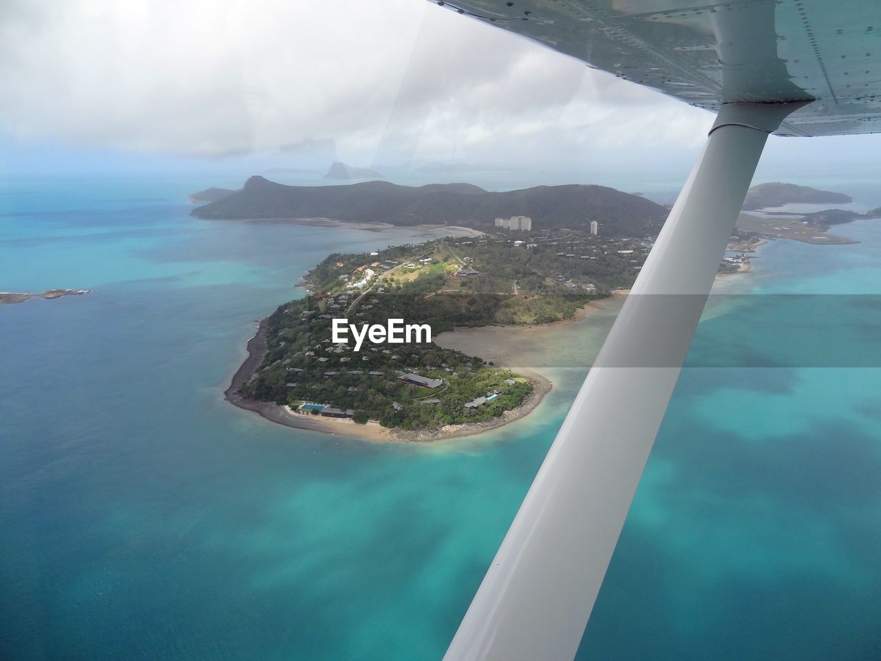 Cropped image of airplane over ocean and island