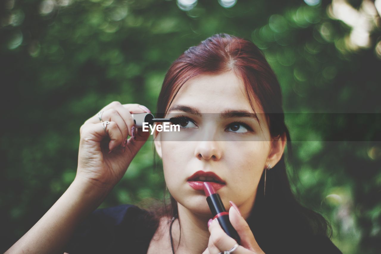 Close-up of young woman looking up while applying makeup on face