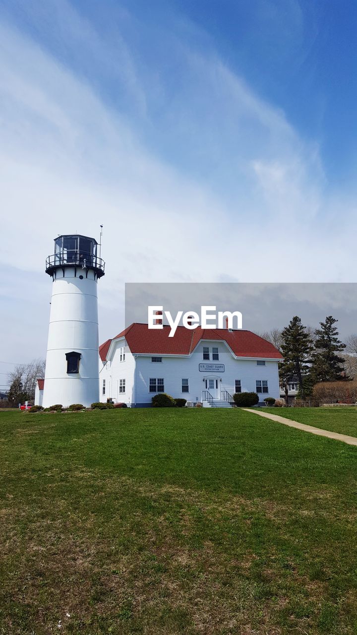 Lighthouse on field by building against sky