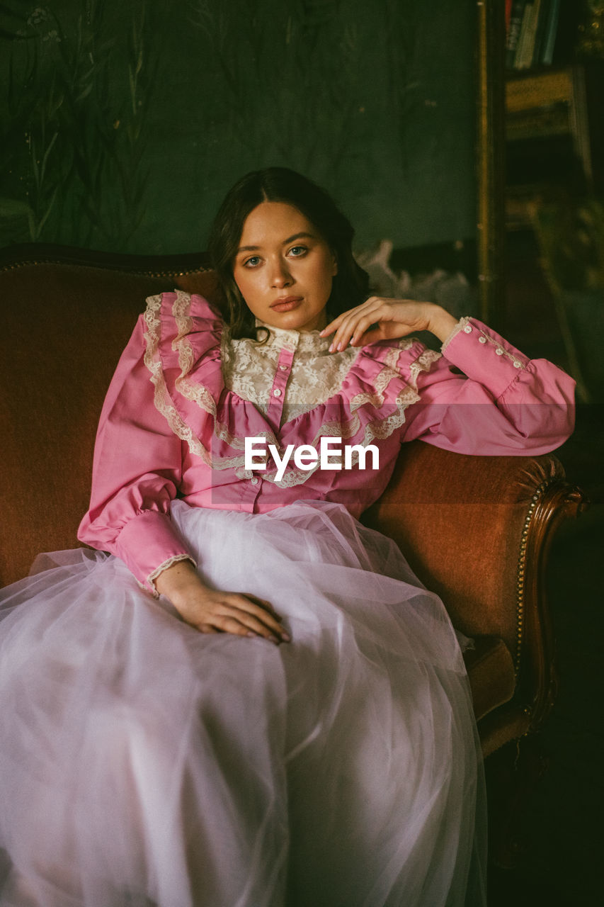 Portrait of young woman sitting on pink indoors