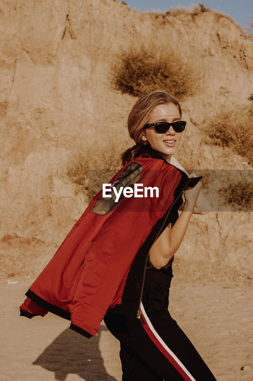 Portrait of young woman wearing sunglasses while standing against mountain