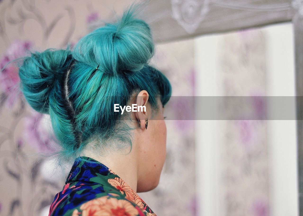 Young woman with dyed hair by mirror at home