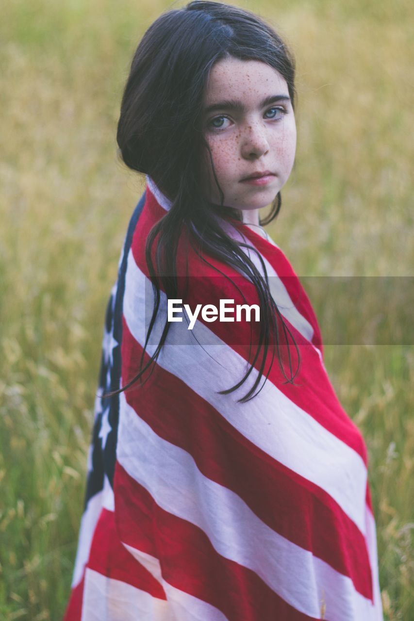 Portrait of girl wrapped in american flag while standing on field
