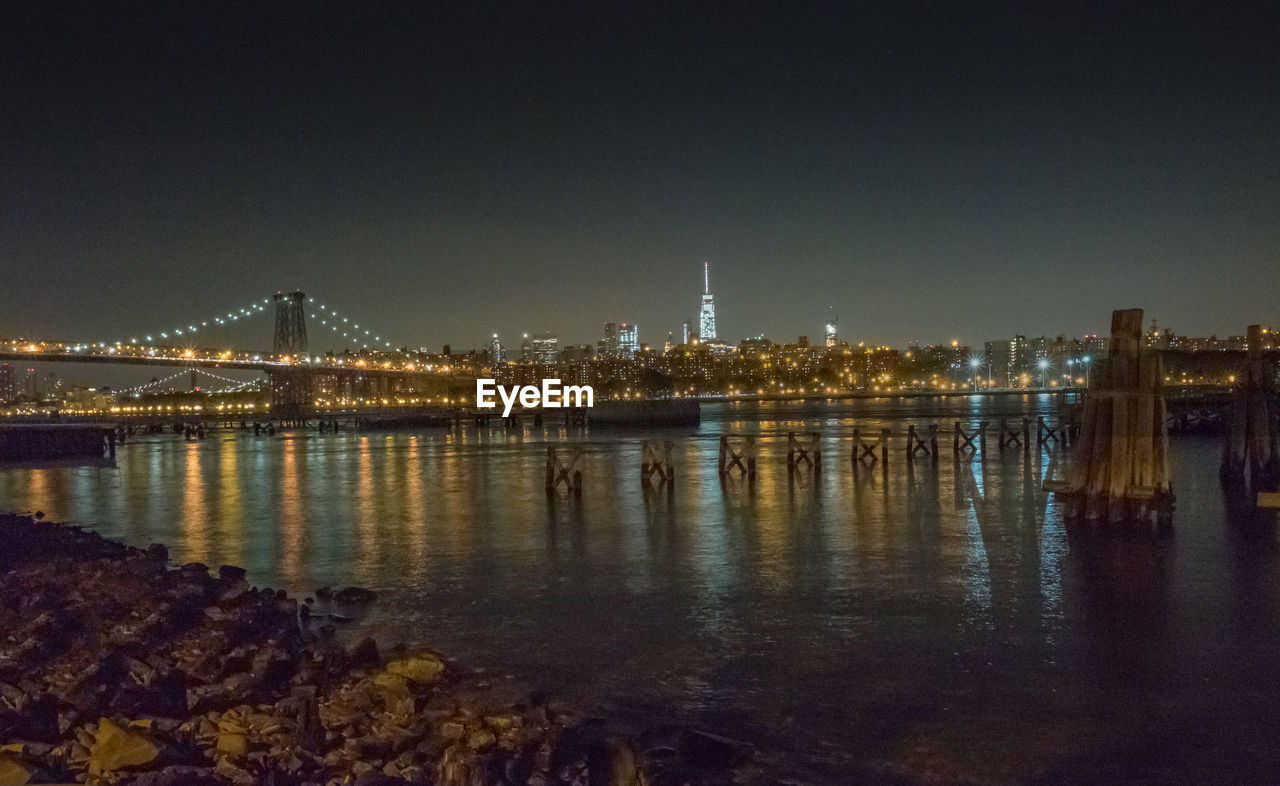 Illuminated bridge over river by city against sky at night