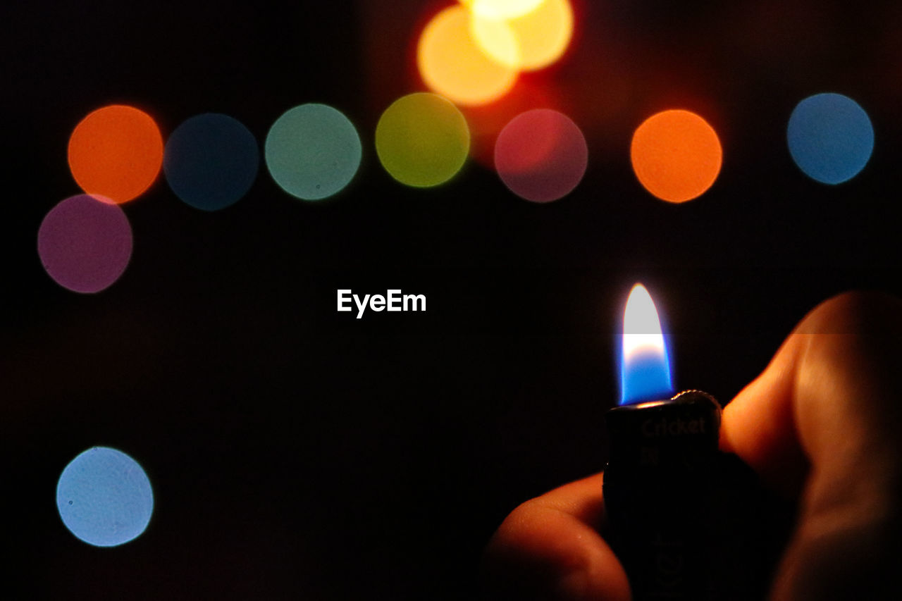 Close-up of hand holding cigarette lighter against blurred backgrounds