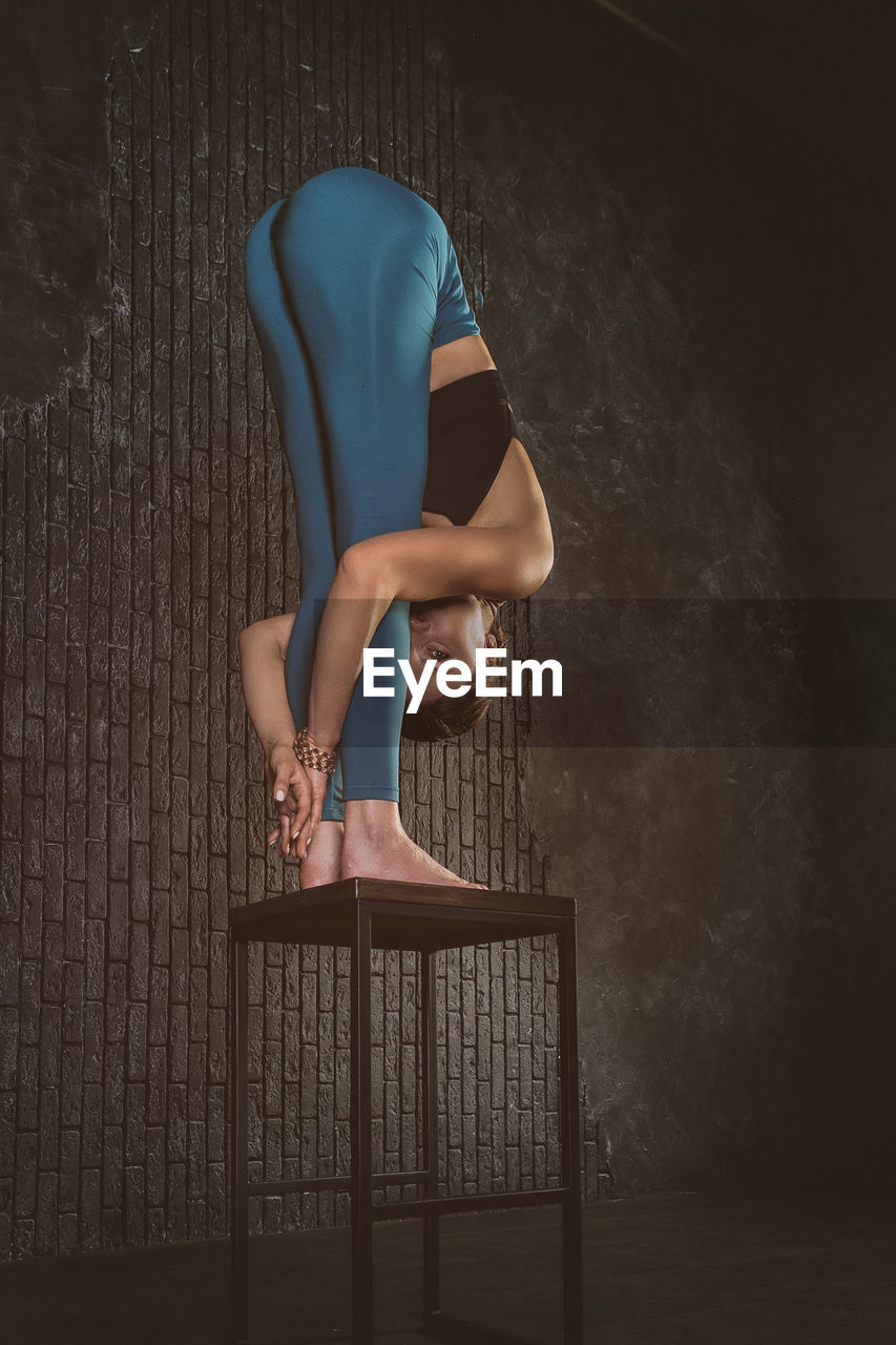 A charming girl in a sports uniform does yoga in an old room with a fireplace and candles