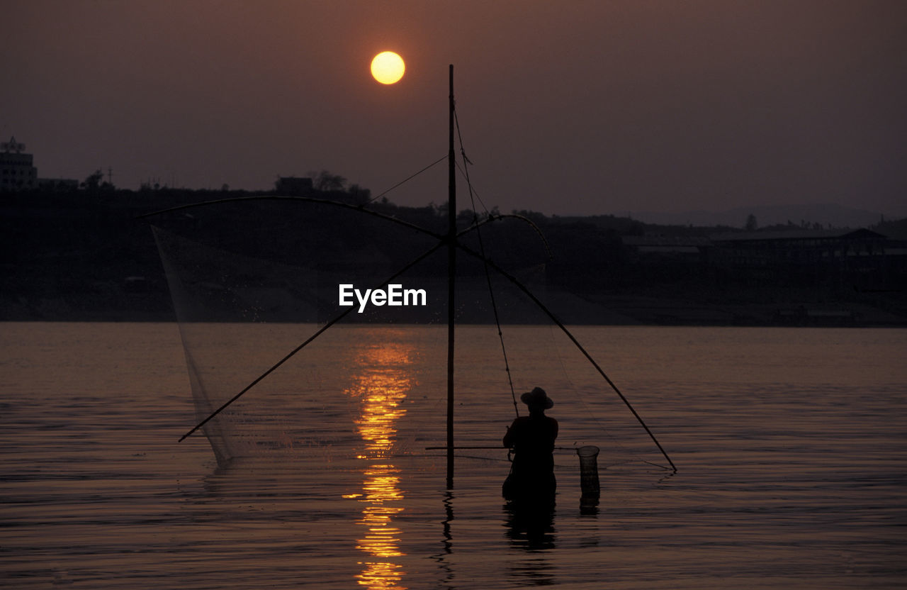 Silhouette man fishing in lake against sky during sunset