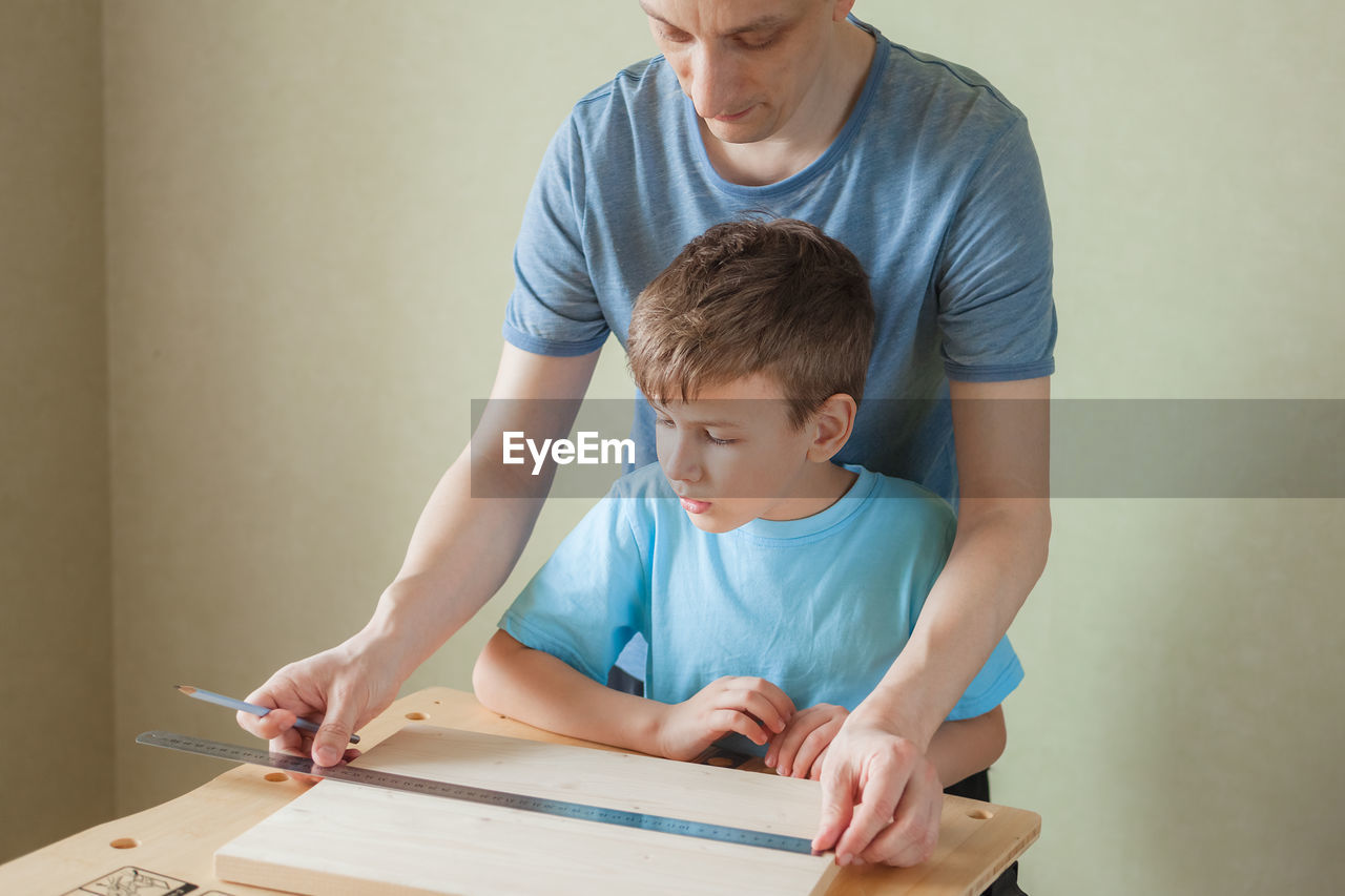 Cute little boy with pencil in hand making marks on wooden plank. father teaches son carpentry