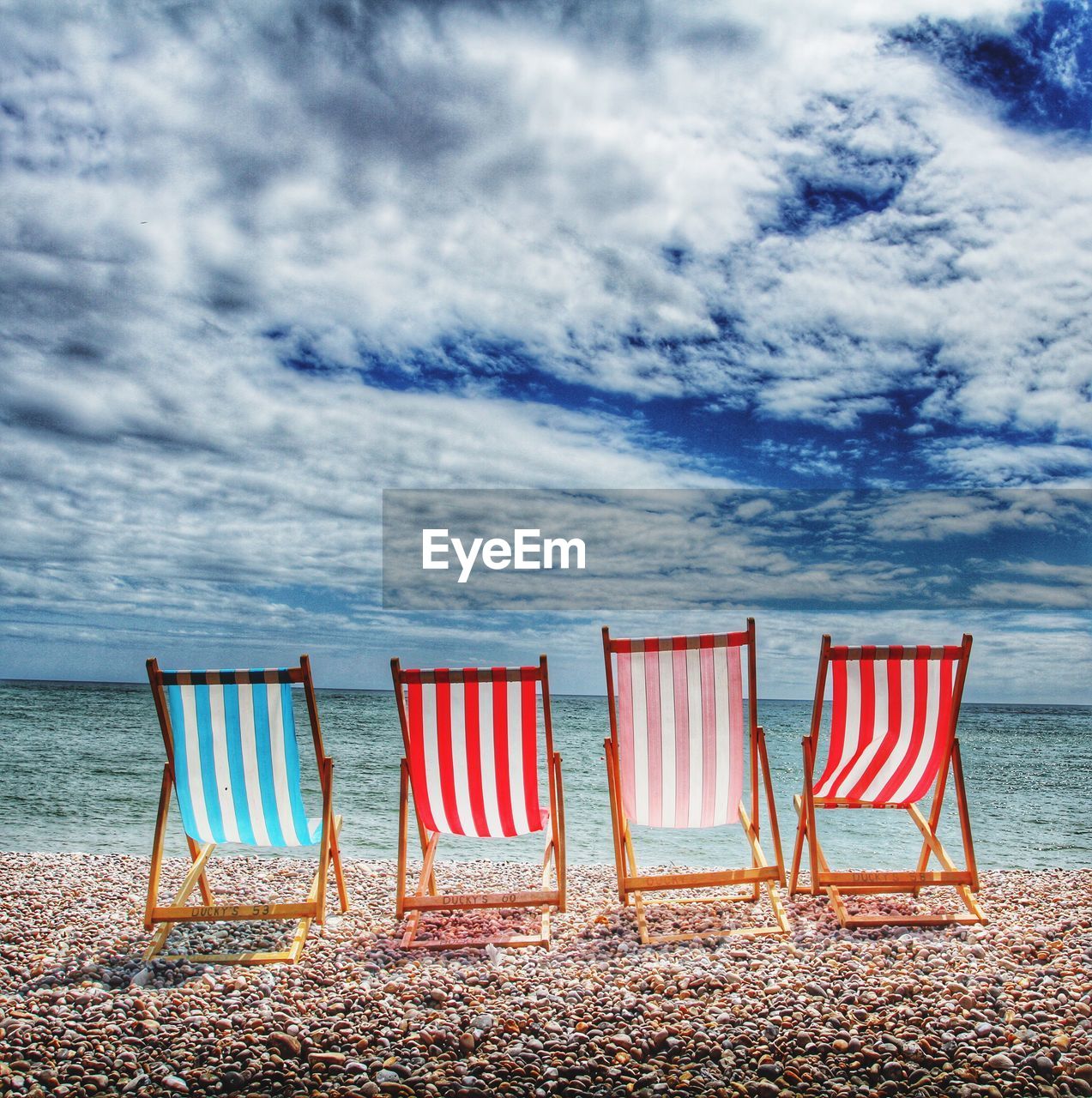 Deck chairs at sea shore against cloudy sky