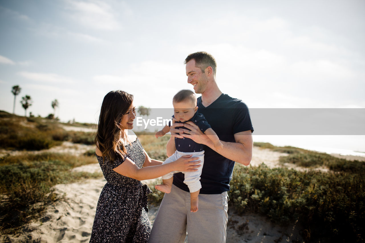 Mother & father smiling & holding infant son on beach