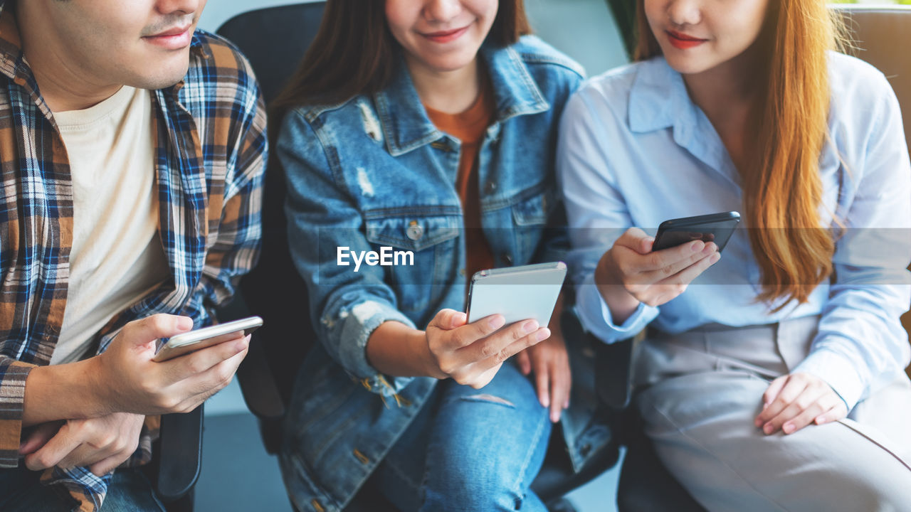 midsection of friends using phone while sitting