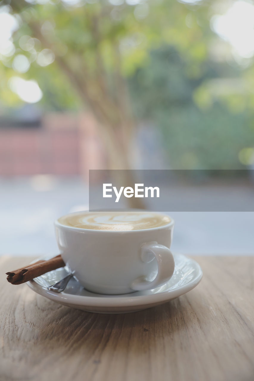 CLOSE-UP OF COFFEE CUP ON TABLE AGAINST BLURRED BACKGROUND