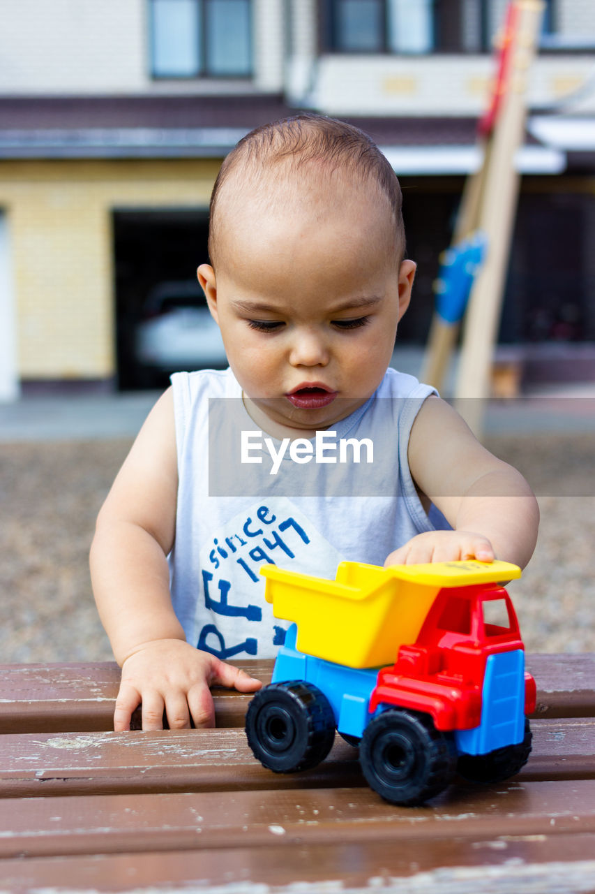 Cute pretty little baby baby plays with toy car on children playground
