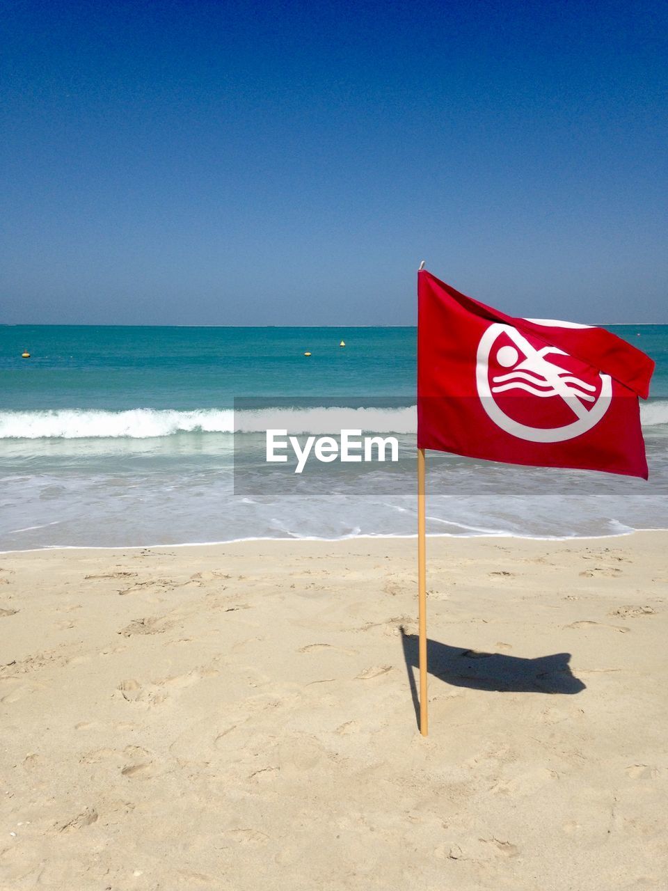 Red flag on beach against clear blue sky