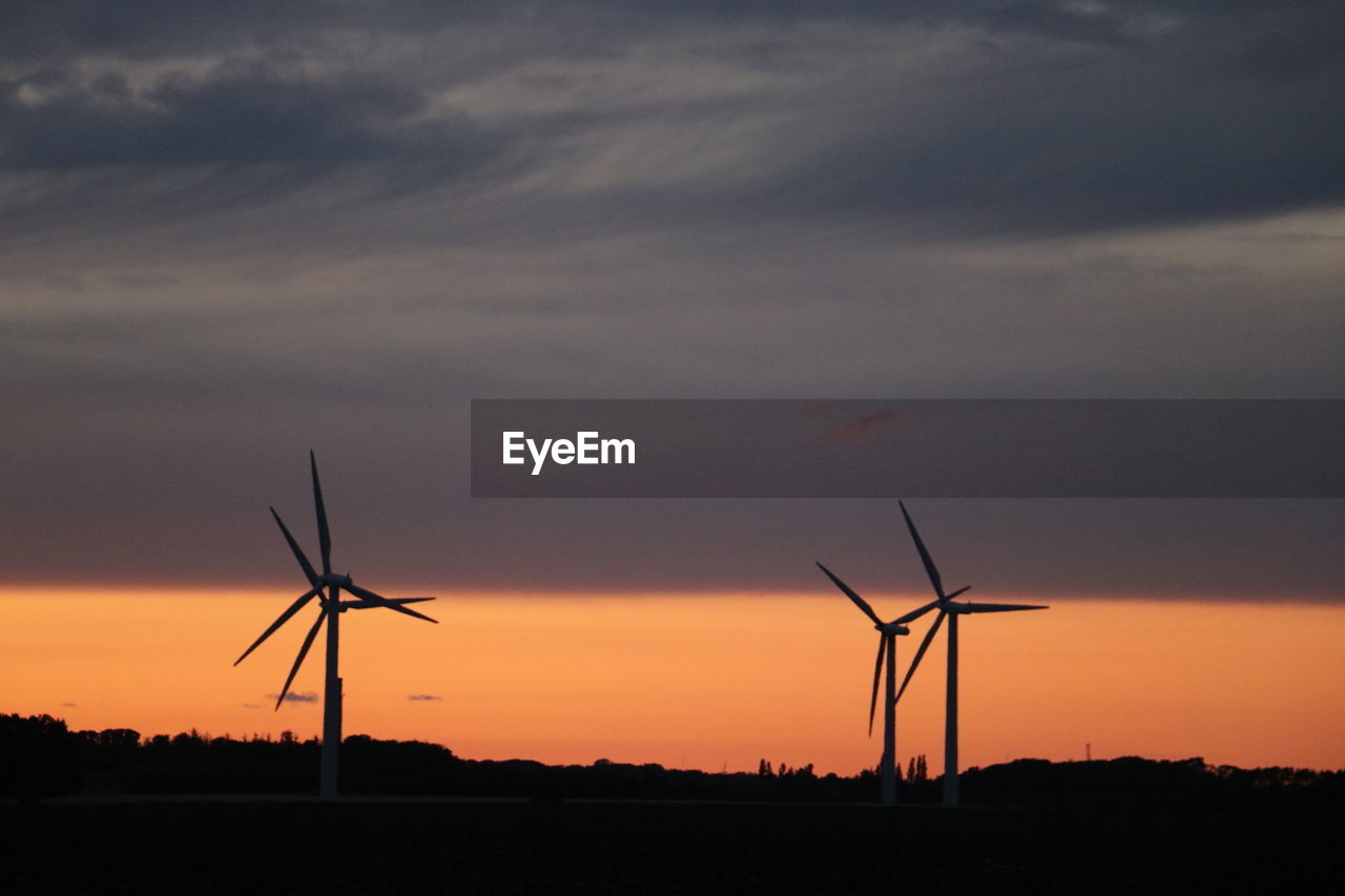 Silhouette wind turbines on field against sky during sunset