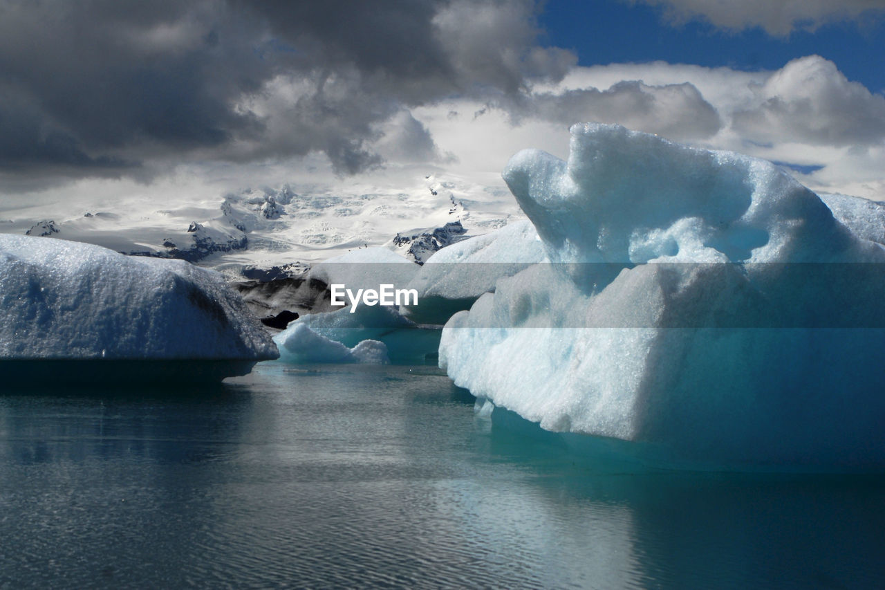Scenic view of glaciers in lake against cloudy sky during winter