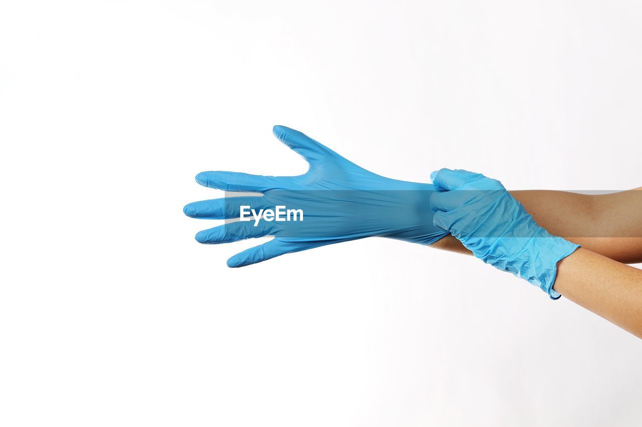 Cropped hands of person putting on surgical gloves against white background