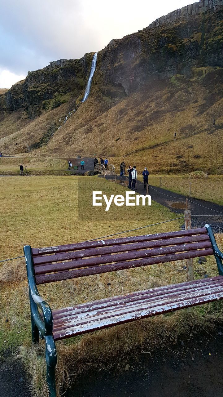 PEOPLE ON FIELD BY MOUNTAIN AGAINST SKY