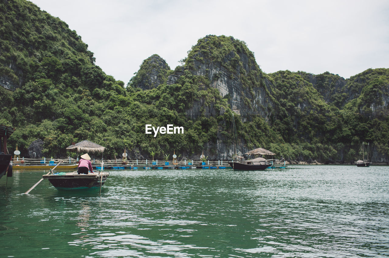 Rear view of woman standing in rowboat on halong bay by mountains