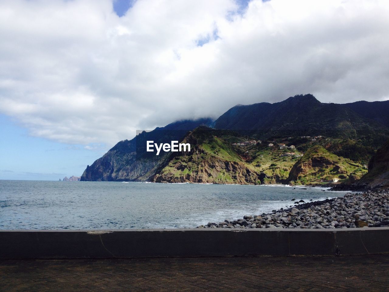 Scenic view of sea by mountains against cloudy sky