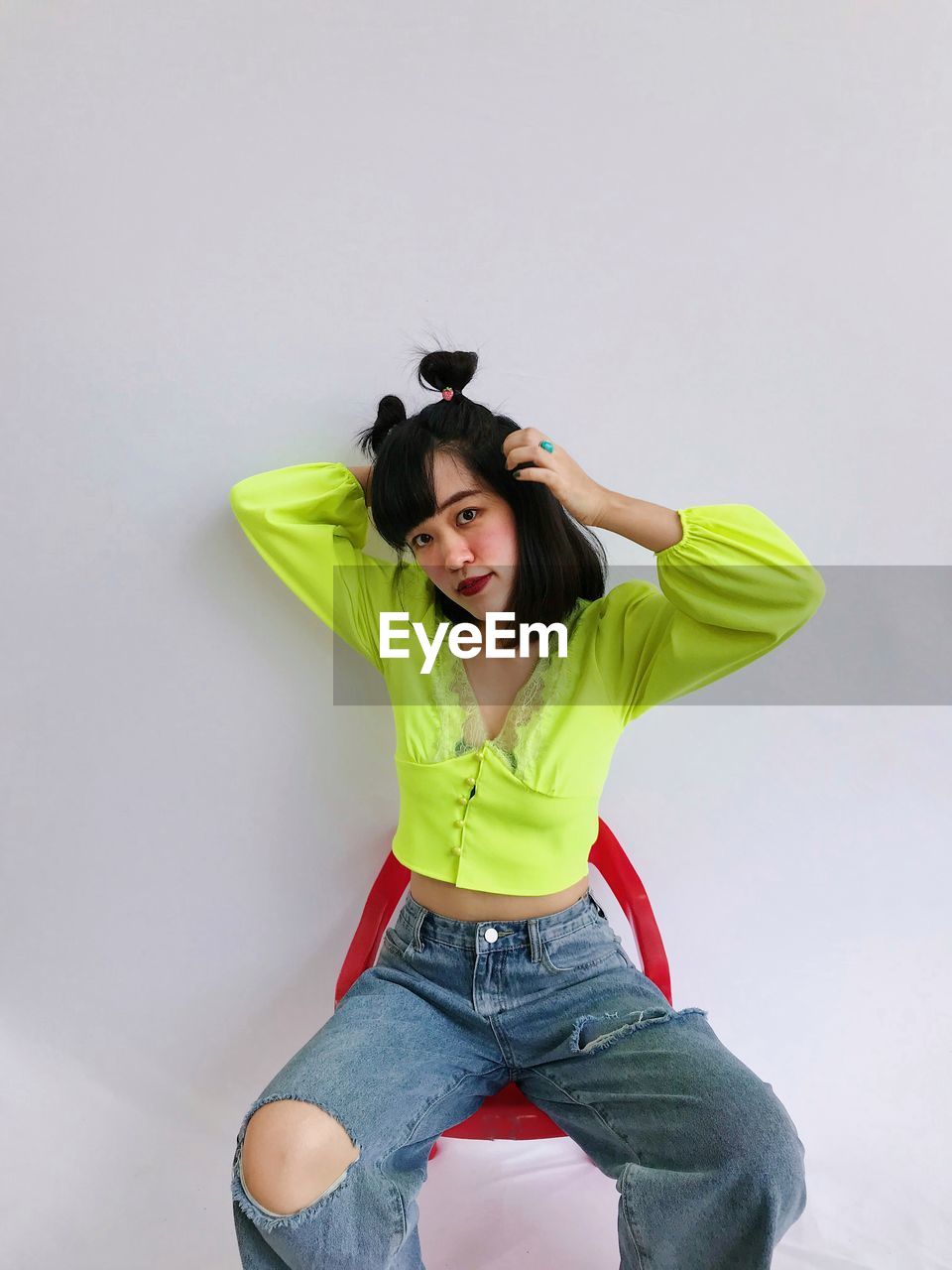 Portrait of asian woman in chartreuse top sitting in a red chair over white background