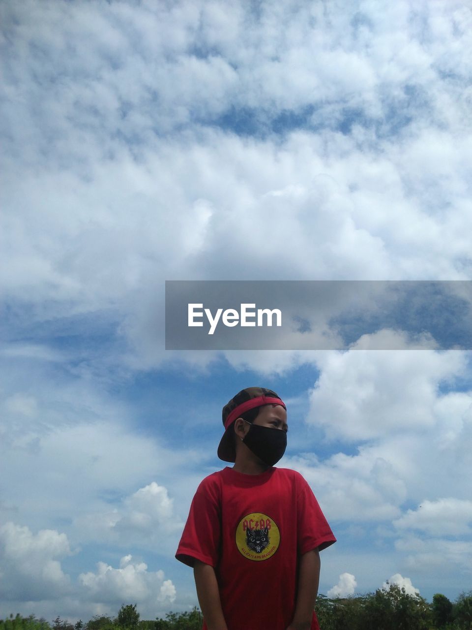 LOW ANGLE VIEW OF BOY STANDING AGAINST THE SKY