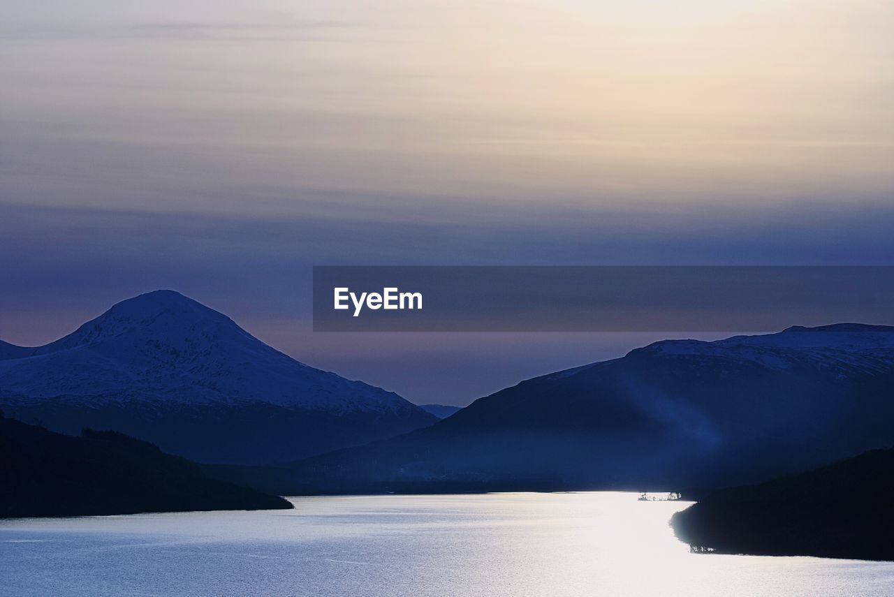 Scenic view of river and mountains against sky during sunset