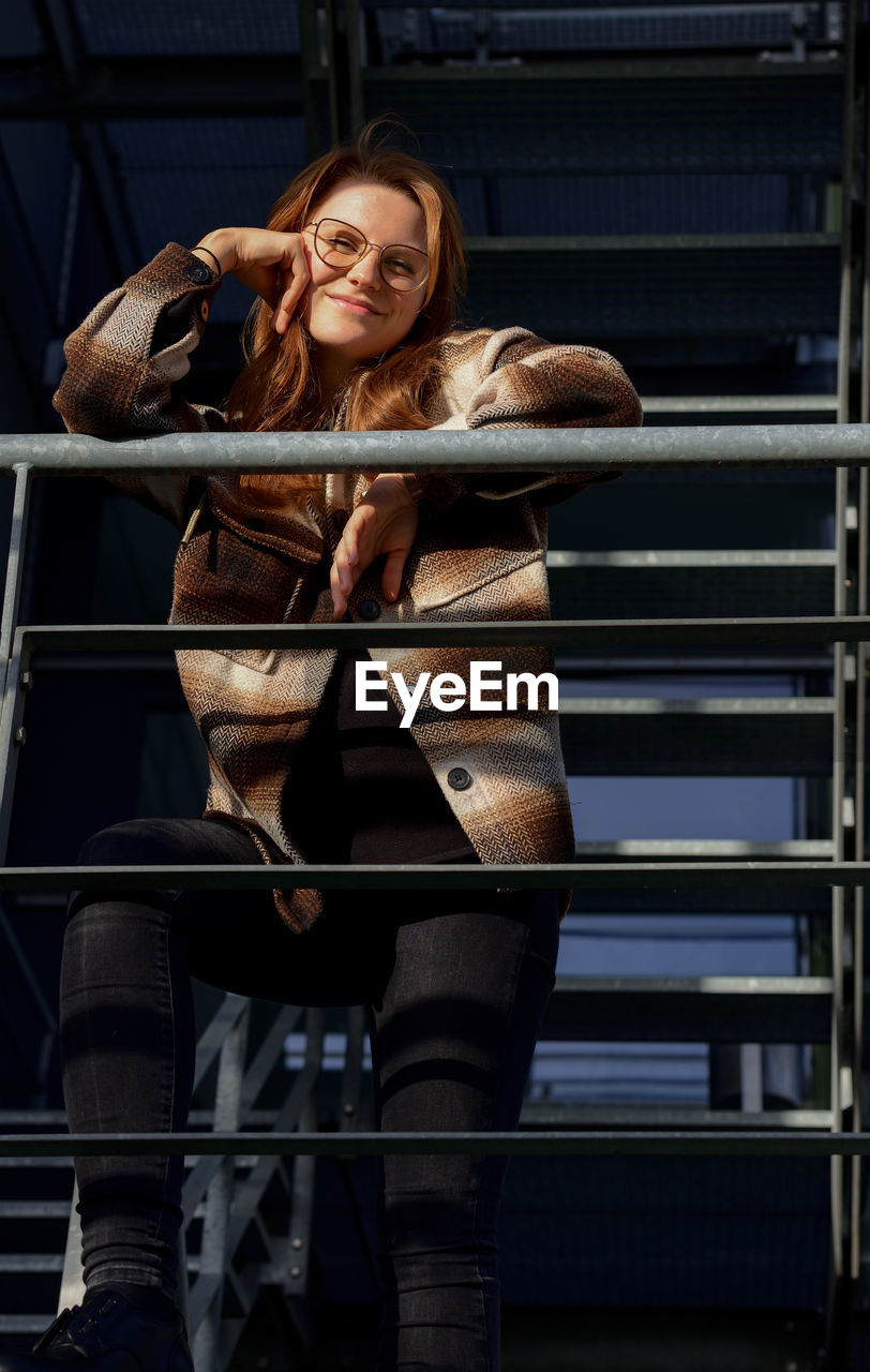 Portrait of young smiling woman standing against railing