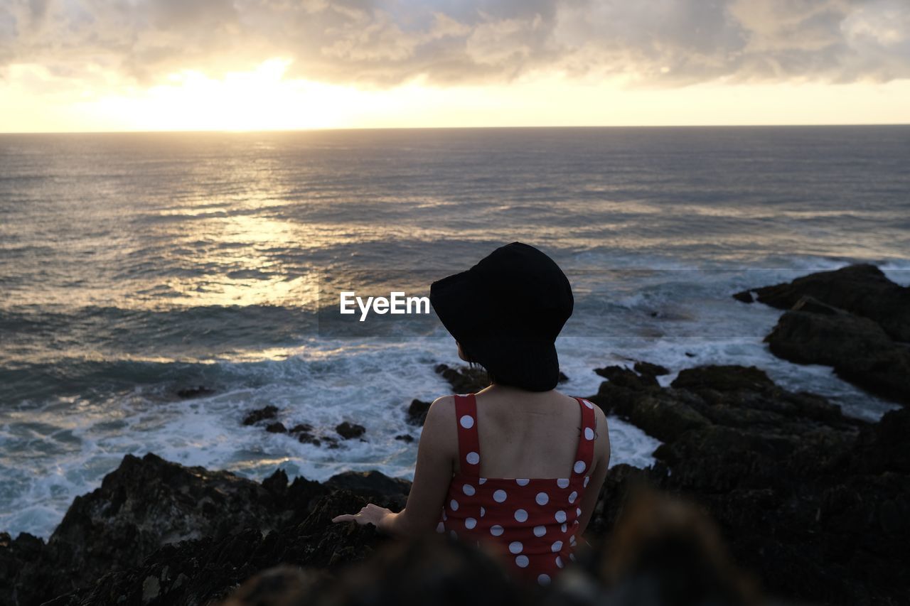 rear view of woman standing on rock at sunset