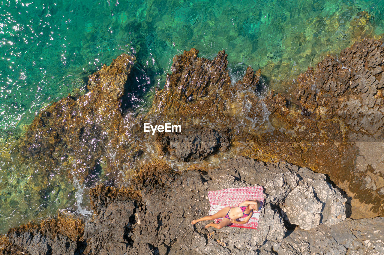 Aerial view of a girl sunbathing on the rocky beach,  adriatic sea in croatia