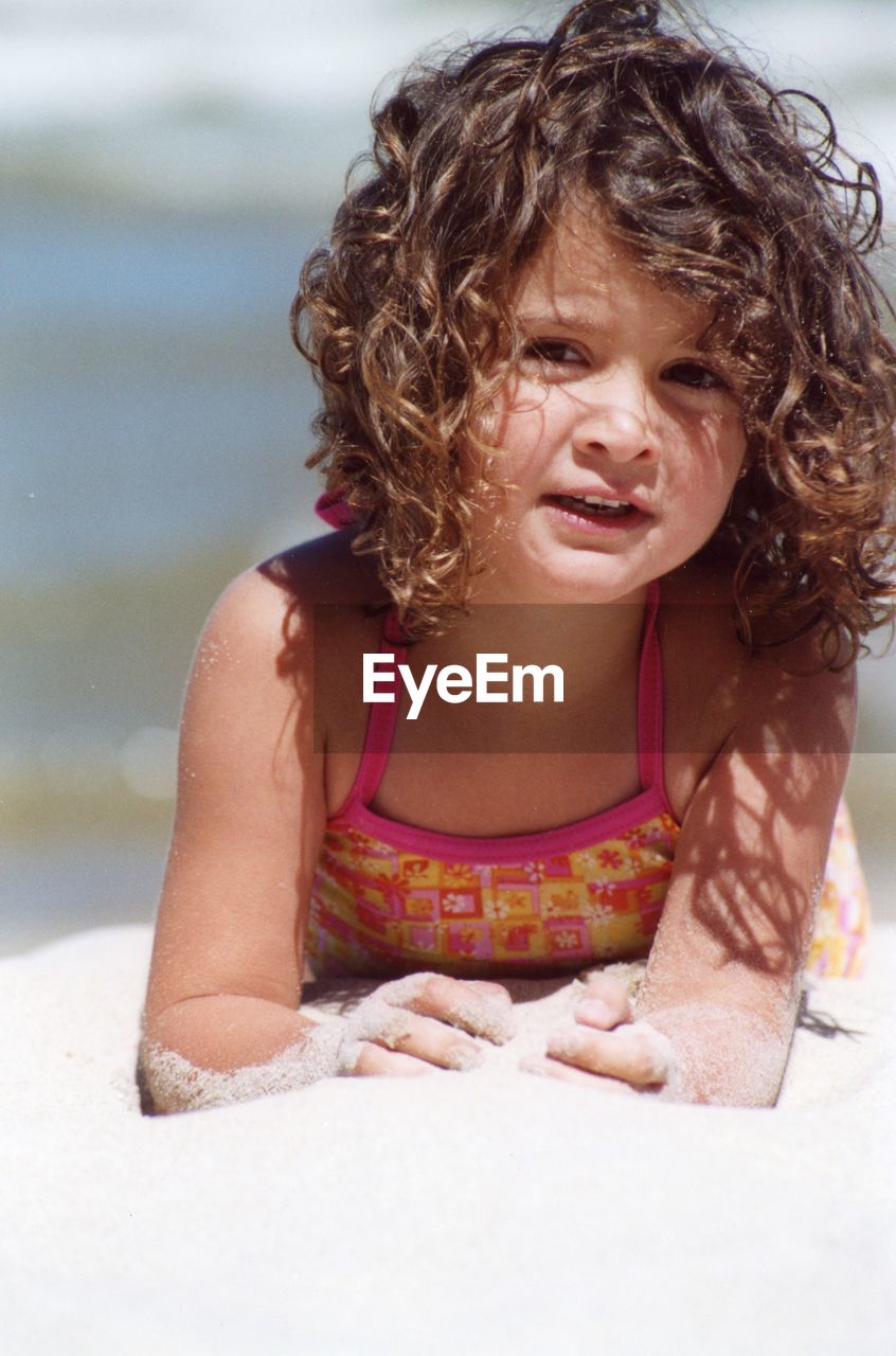 Close-up of smiling girl lying on sand at beach