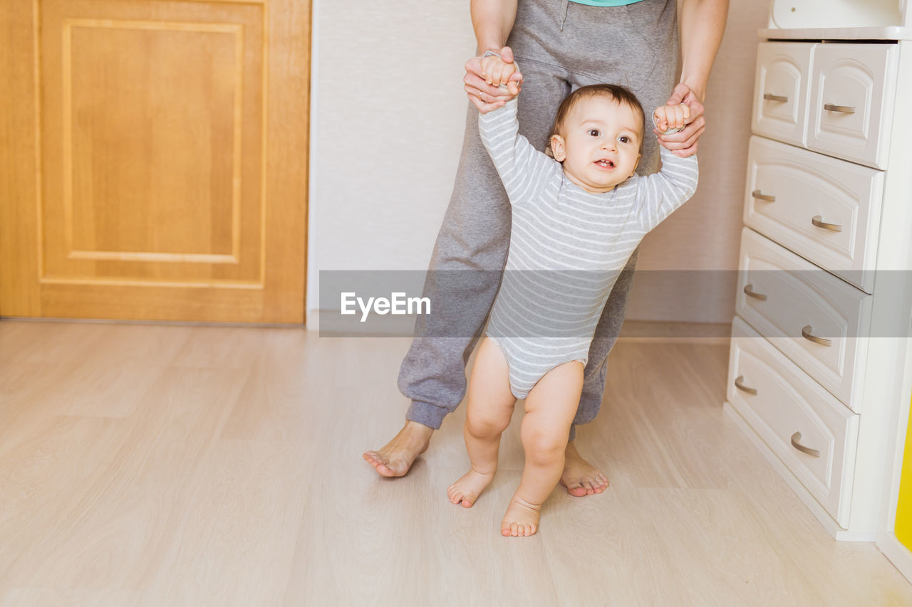 Low section of mother with baby standing on floor at home