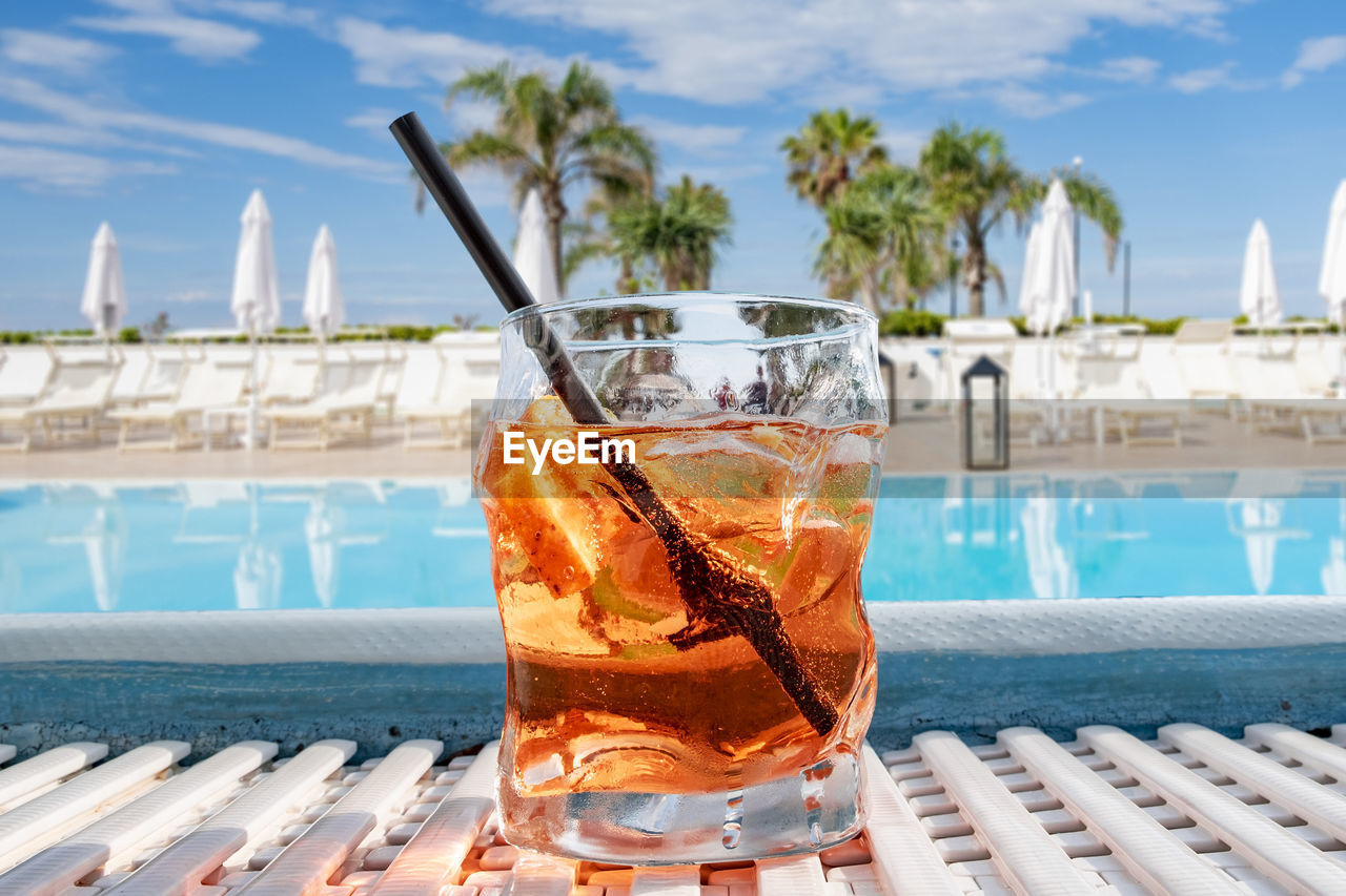 Close-up of drink on table by swimming pool against sky