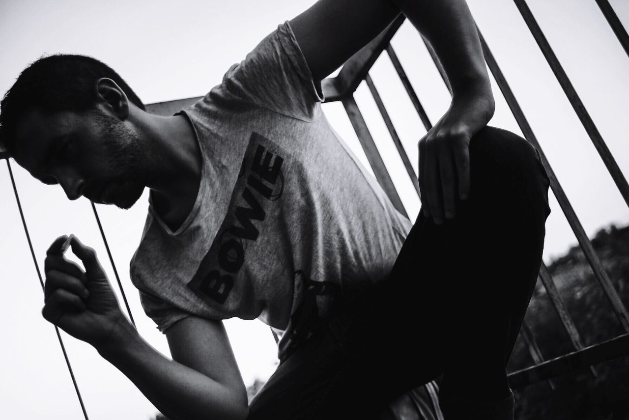 Low angle view of man crouching against railing