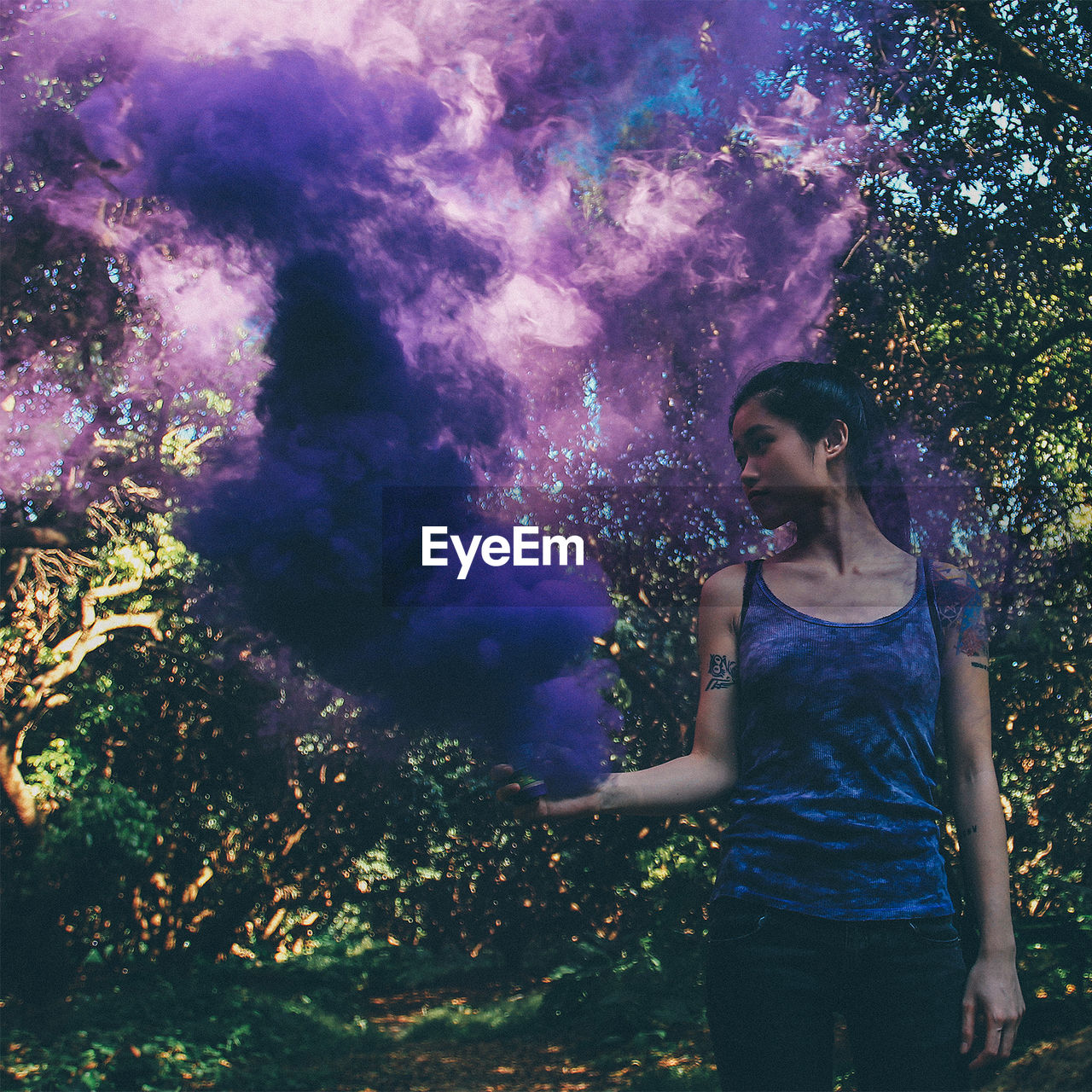 Young woman with purple smoke bomb in forest