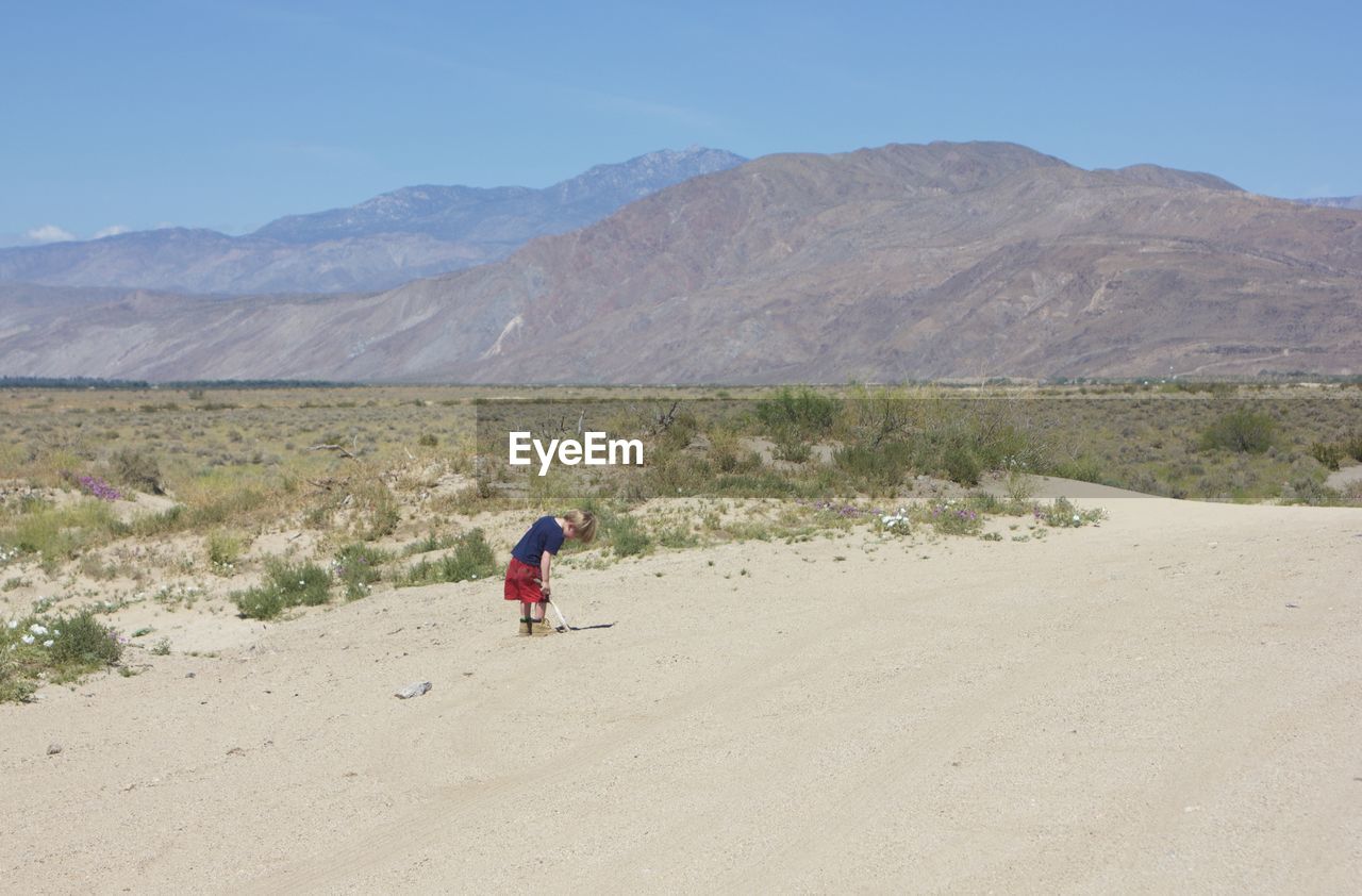 Side view of boy standing at desert against sky