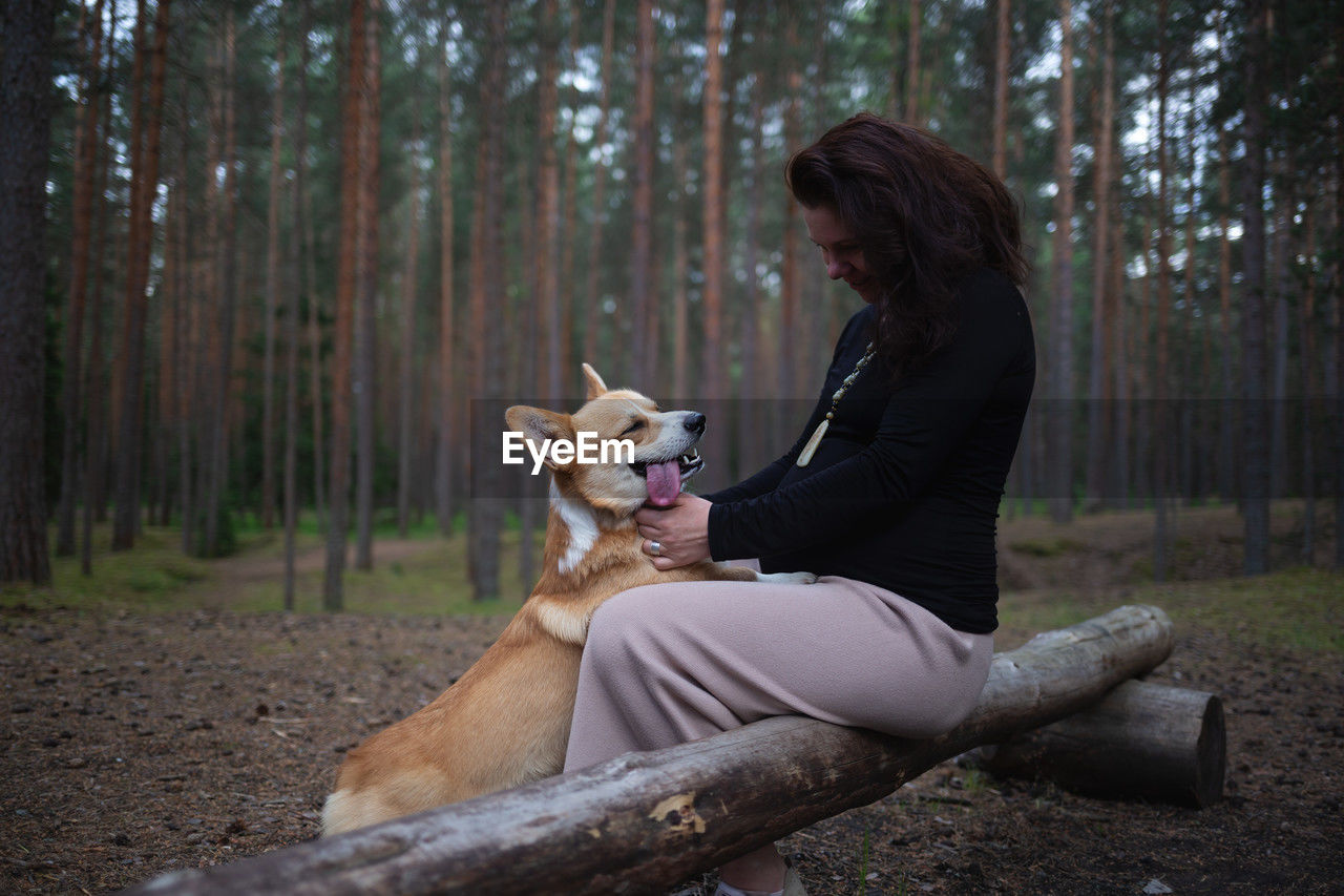 side view of young woman with dog standing in forest