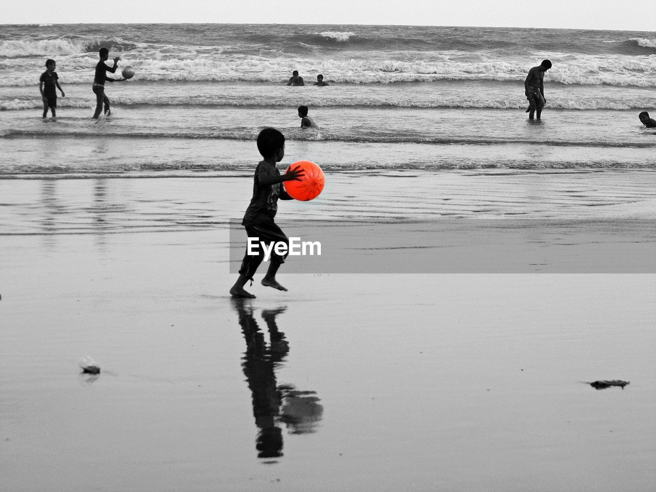 Boy playing with red ball while walking on sea shore