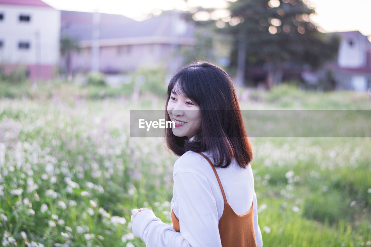 Side view of happy young woman on flowering field during sunny day