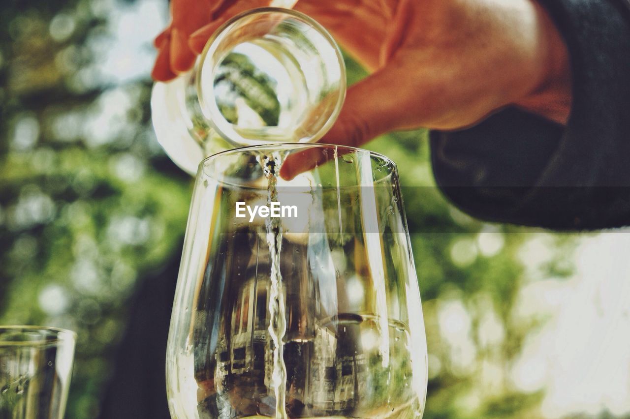 Cropped hand pouring water from jar in glass