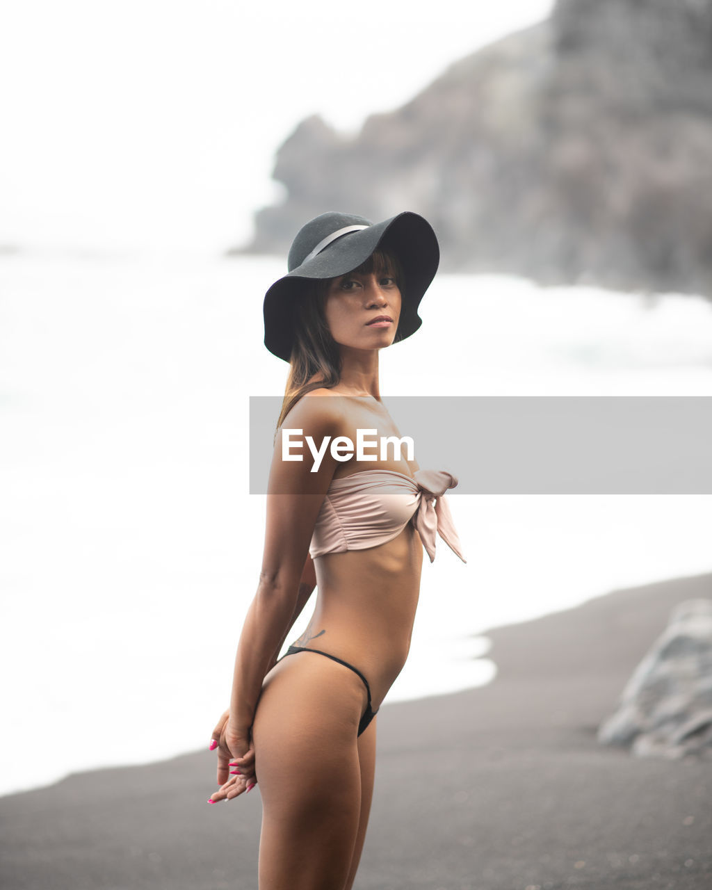 side view of young woman sitting on rock at beach against sky