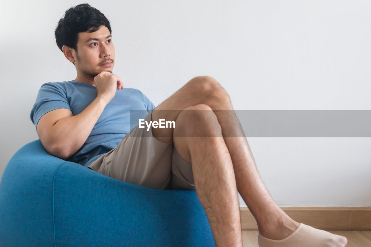 View of man's legs on white bed with tv and plant.