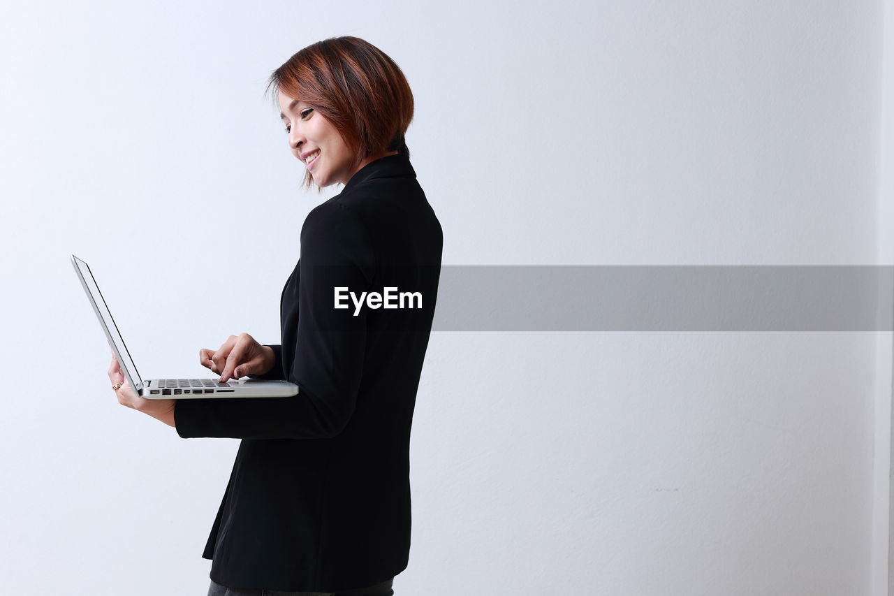 Side view of businesswoman using laptop while standing against white background