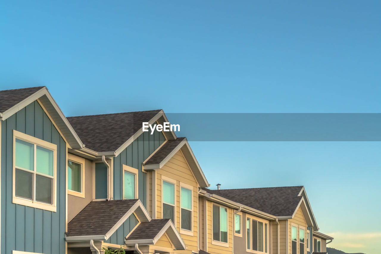 LOW ANGLE VIEW OF HOUSES AND BUILDINGS AGAINST CLEAR BLUE SKY