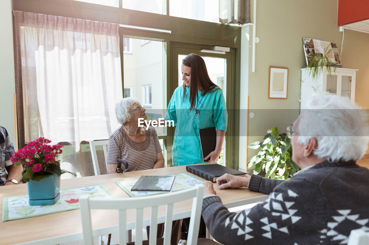 Young nurse talking with senior woman sitting at table in nursing home