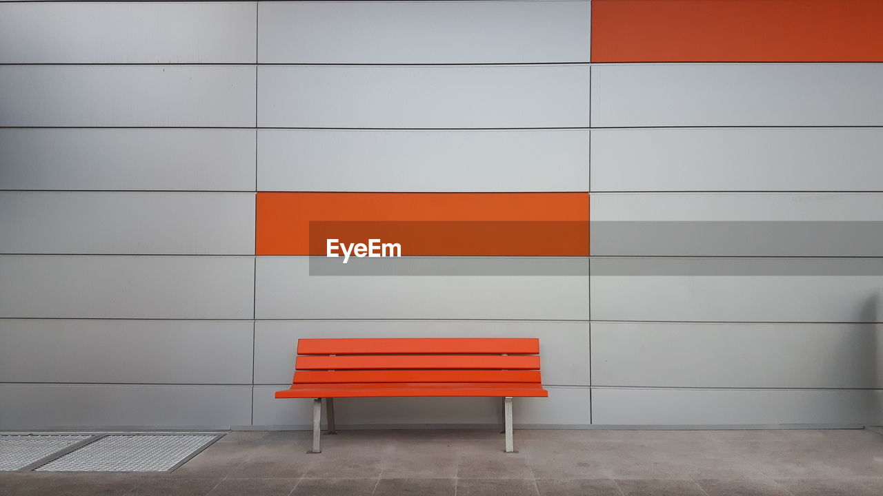 Empty orange bench against gray wall