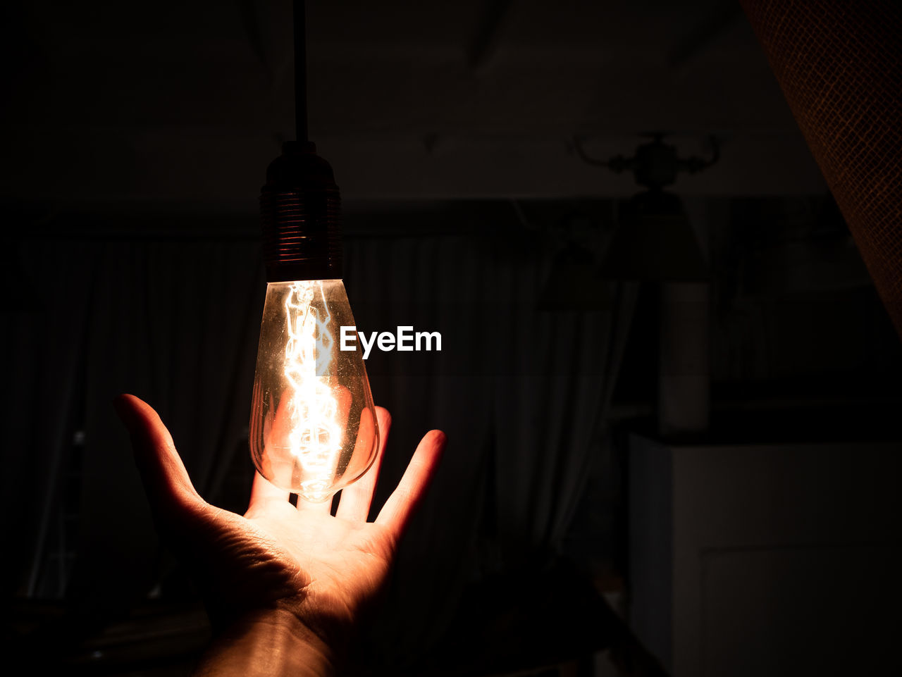 HUMAN HAND HOLDING LIGHT BULB AGAINST DARK BACKGROUND